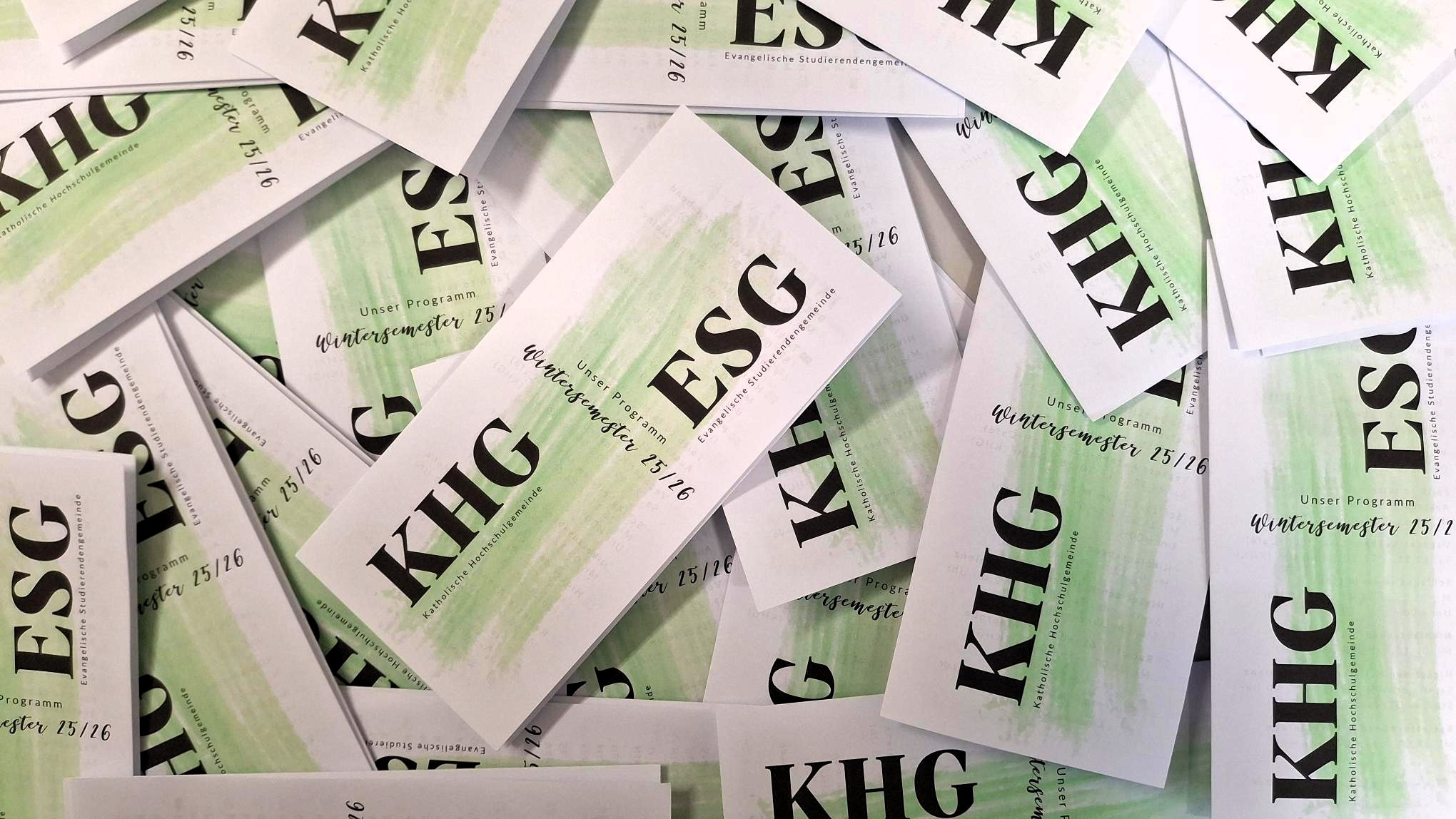 KHG-Programme des Wintersemesters 2025-2026 liegen durcheinander auf einem Tisch